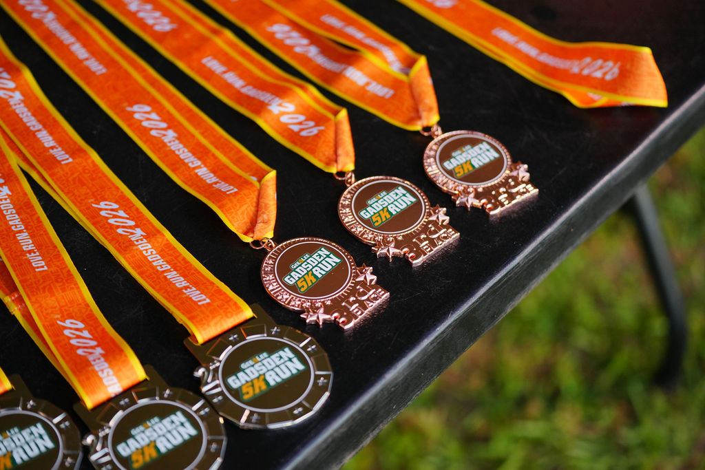 Gadsden 5K finisher medals with orange ribbons laid out on a table